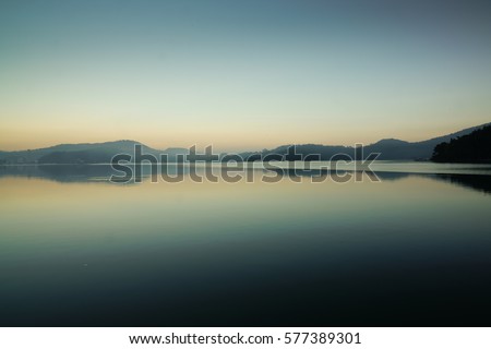Reflection of mountain range in clear and still water at the Famous Sun Moon lake in Taipei depicting peaceful morning. This Beautiful landscape with Sunrise at dawn is a popular tourist attraction. Stockfoto © 