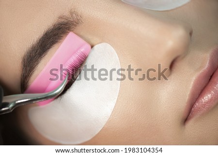 Master glues eyelashes to pink lash roller. Close-up of beauty model's face during lash lift laminating botox procedure. Eyelash Care Treatment: lifting and curling, lash lamination and extension.