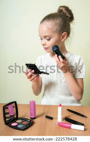 Fashion little girl applying make up. Mascara, eye shadow, lip gloss, lipstick, powder.  Place for text.