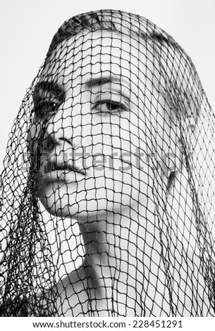 Portrait of an attractive  blond model covered by the net. Net, trap, trouble concept. Black and white.