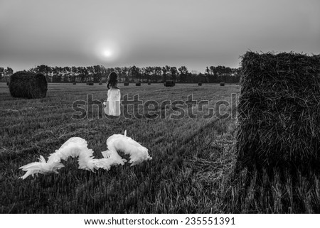 beautiful girl is running away from the angel wings  on the field in the morning. Black and white