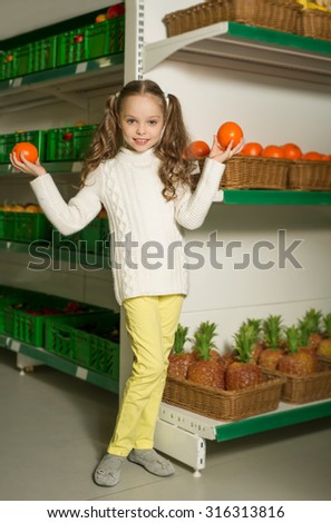 Beautiful little girl with orange in their hands at the toy supermarket. plastic fruits on shelves.