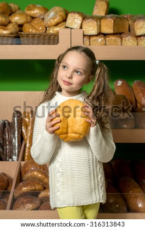 Little girl with bread in hand front of shelves with a variety of bread. Supermarket or bread shop.
