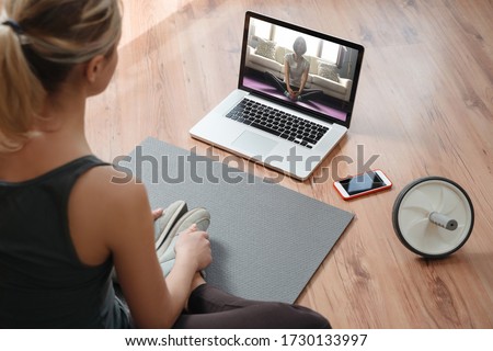 Yoga teacher conducting virtual class at home on a video conference. Young beautiful woman doing an online yoga class in her living room with laptop. Home fitness and workout concept