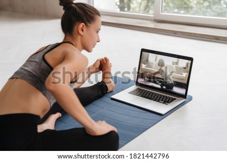 Fit woman in sportswear doing yoga on exercise mat at home using laptop watching tutorial. Female coach has a virtual yoga class on computer. Healthy and active lifestyle concept. Online home training