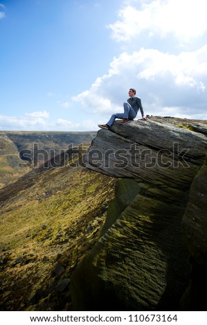 Young man sitting on cliff\'s edge and looking to a sky with clouds