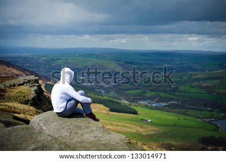 Man with hood sitting on cliff and looking to a view