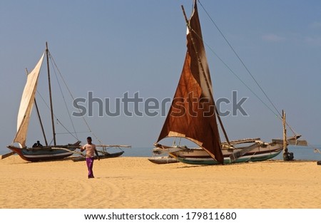 NEGOMBO, SRI LANKA - FEBRUARY 12: A man walking on the sand with fishing boats behind him on the beach in Negombo, Sri Lanka on the 12th February, 2014.