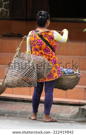 LUANG PRABANG, LAOS - AUGUST 15th: A common sight of a hill tribe woman carrying live poultry and fruit in baskets over her shoulder in Luang Prabang, Laos on the 15th August, 2014.