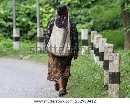 LUANG PRABANG - AUGUST 16: A local hill tribe woman walking along the road with a typical bag slung around her forehead near Luang Prabang, Laos on the 16th August, 2014.