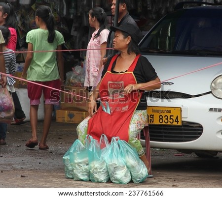 VIENTIANE, LAOS - AUGUST 6: A local woman with her shopping leaning on a car at the outdoor markets in Vientiane, Laos on the 6th August, 2014.