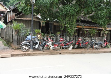 LUANG PRABANG, LAOS - AUGUST 14: A typical scene of motor bikes and men on the roadside in the Unesco town of Luang Prabang, Laos on the 14th August, 2014.