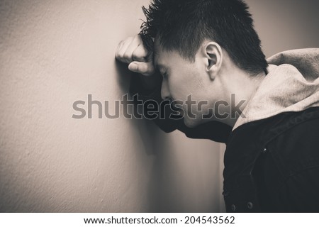 Depressed asian man with fist clenched leaning his head against a wall