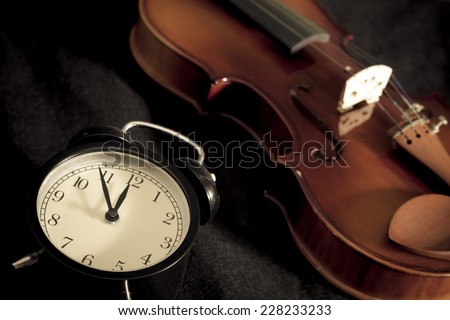 Low key image of alarm clock & old aged classical violin on black fabric / \
