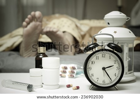 feet of sleeping man in bed with tablets and drugs suffering insomnia, hangover and headache at night