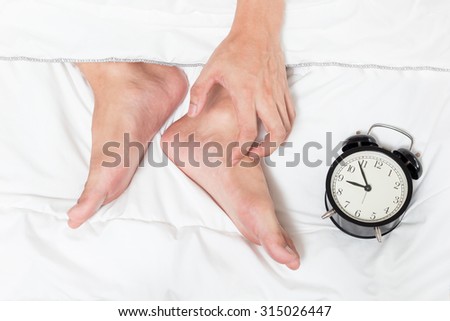 feet of lazy man on white bed & alarm clock. wake up late
