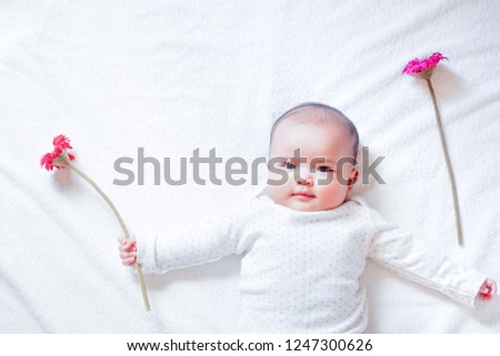 Asian baby girl is holding red and pink flowers on white towel background with sun light shading. Baby girl is plaing with red and pink flower. Baby is happy with her flowers. Zdjęcia stock © 