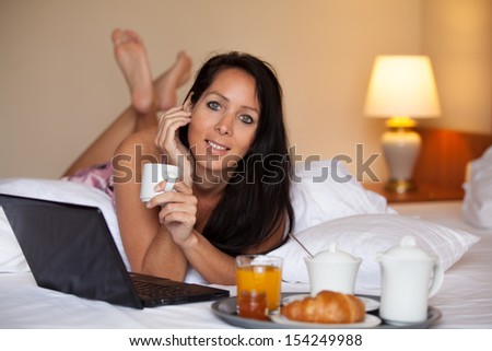 Woman is having breakfast on the hotel bed and surfing at the internet
