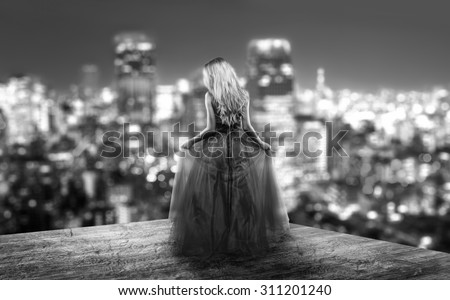 Beautiful woman in a cocktail dress is standing on the top of an skyscraper