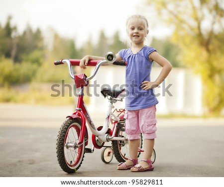 little girl with her hand on the steering wheel stands next to a bicycle