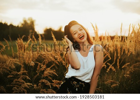 Gorgeous woman in a wheat field on a sunset background. A fashionable girl with long hair rejoices, laughs, enjoys life and summer, nature, happiness. Model in a hat in the forest.