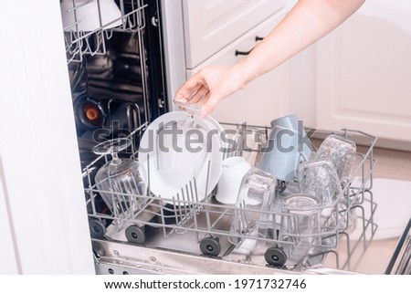 Built-in dishwasher, dishwashing. A woman loads washed dishes, cups, glasses. A woman's gentle hand puts something in the dishwasher or pulls out, unloads.