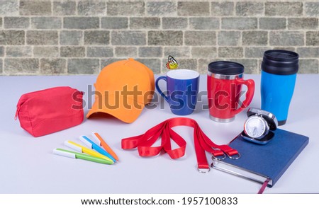 Composition of different promo products with rich colors -Thermo mugs, Lanyards Neck Strap, pens, mug, silver table office clock, zipped coin purse fabric, notebook,cap On desk grey and background gre