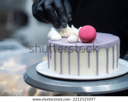 frosted drip cake on stand while designer works on topping Stock fotó © 