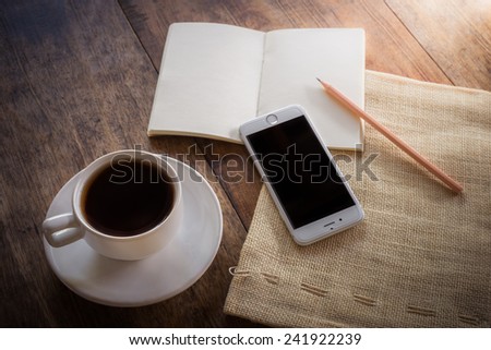 Cup of coffee on a wooden table with glass of water on the Sackcloth bags and smartphone and notebook and pencil. Simple workspace or coffee break with web surfing