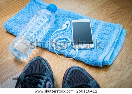 Sport equipment. Sneakers, water , earphones, smart phone on wooden background