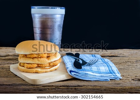 chicken hamburger and glass of cola on wooden cutting board with Knife and fork, napkin on top wooden table