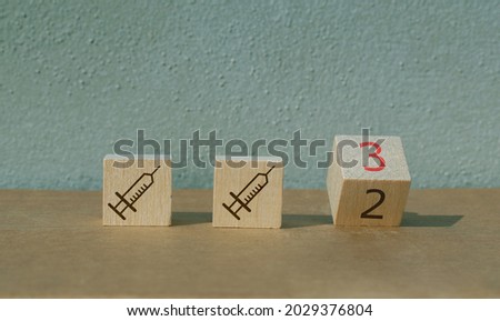 Illustration of booster shot for mRNA vaccines for Covid-19 with wooden block flipping from 2 to 3. Two wooden blocks with syringes.