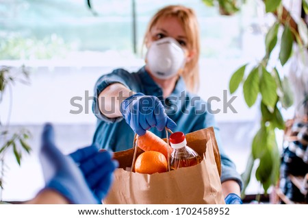 Woman delivering Food in paper bag during Covid 19 outbreak. Female  Volunteer holding groceries in the house porch. Delivery woman in face mask and gloves giving Donating neccessities to a hand Foto d'archivio © 