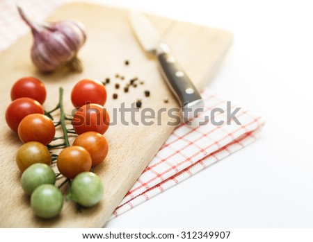 Tomatoes cherry with garlic and black pepper on the wooden board. Different degrees of ripeness of tomatoes cherry. Isolated on white
