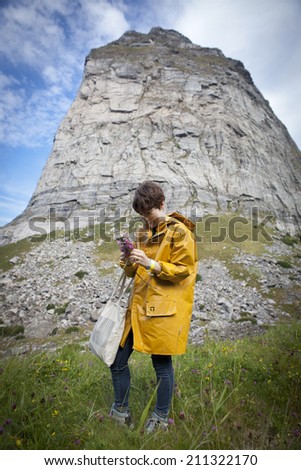 Traena, Norway - July 12 2014: during the Traena music festival, girl with a yellow rain coat picking flowers before the concert of Norwegian Singer Stein Torleif Bjella on Sanna Island