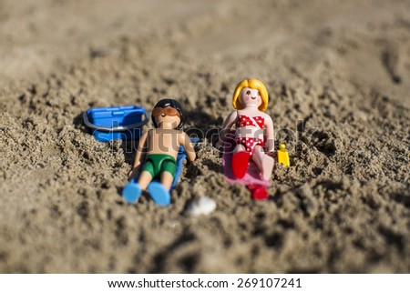 Amsterdam, the Nertherlands. April 12, 2015. A man and a woman sun tanning lying on the sand. Playmobil toy line exist since 1975 and is produced by the German company Brandtaetter.