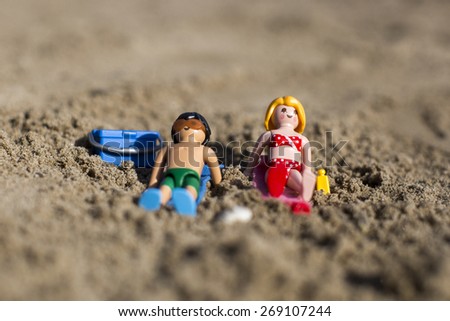 Amsterdam, the Nertherlands. April 12, 2015. A man and a woman sun tanning lying on the sand. Playmobil toy line exist since 1975 and is produced by the German company Brandtaetter.