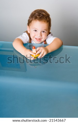 Small smiling boy with a toy on glass table