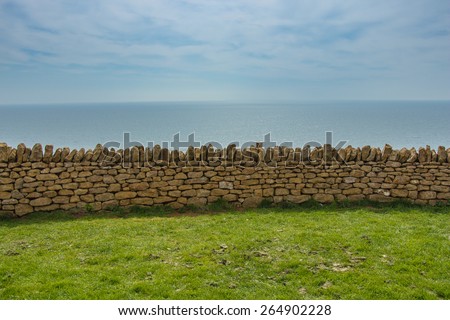 A stone wall separating green lawn from the horizon. Horizontal exposition of four elements: green meadow, stone wall, blue sea and the sky.