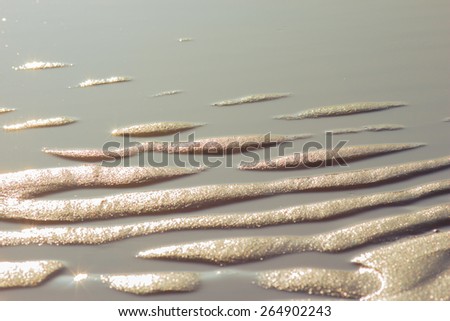 Golden sand revealed by the sea in a still shallow water is sparkling in the evening sun.
