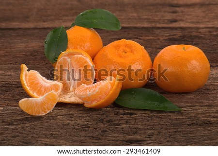 Ripe Mandarin fruit with leaves and one peeled open place on old rustic look timber