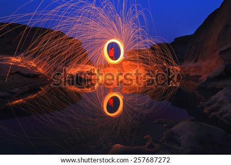 man swing fire on a rock with a water reflection