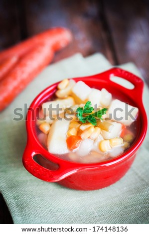 Chicken noodle soup with vegetables in red bowl on rustic table
