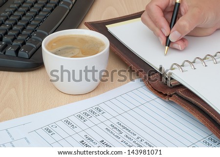 work desk with coffee, accounting sheets and roofing ordered and hand writing in notebook