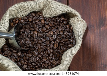 Roasted coffee beans waiting to be ground even in burlap bag on wooden dark table