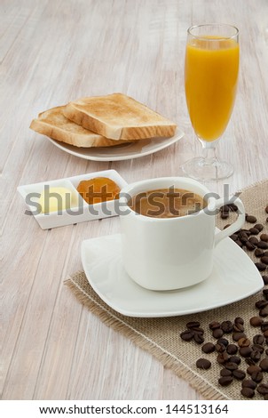 Breakfast with coffee, toast with jam and butter and orange juice on wooden table decorated with white cloth jute coffee beans
