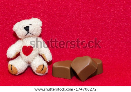 Teddy bear with three heart shaped chocolates on a red background