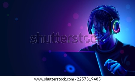 Man working on laptop in the dark room with neon lights. Computer hacker or computer video games gamer or programmer with headset and glasses setting at laptop in darkened room. Computer entertainment