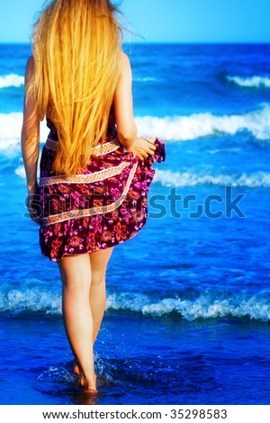 Back of blonde sexy woman walking into the blue sea