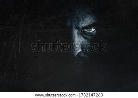 Dark man portrait with scary evil eye. Spooky male face hiding in shadow, creepy frightening expression
